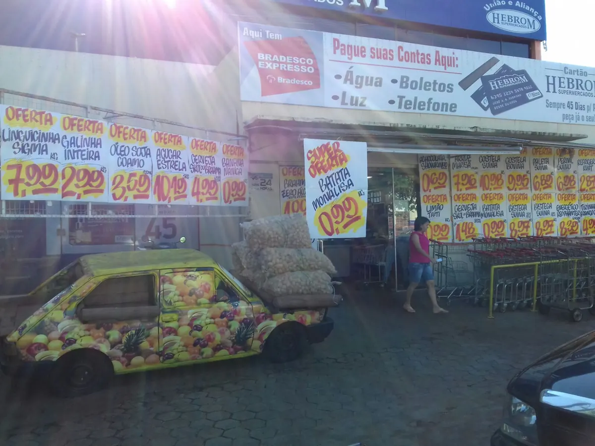 Fachada do Hebrom com cartazes de oferta pintados à mão e carrinhos na calçada