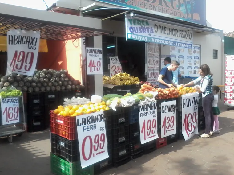 Feirão de frutas e verduras na calçada, com clientes escolhendo produtos